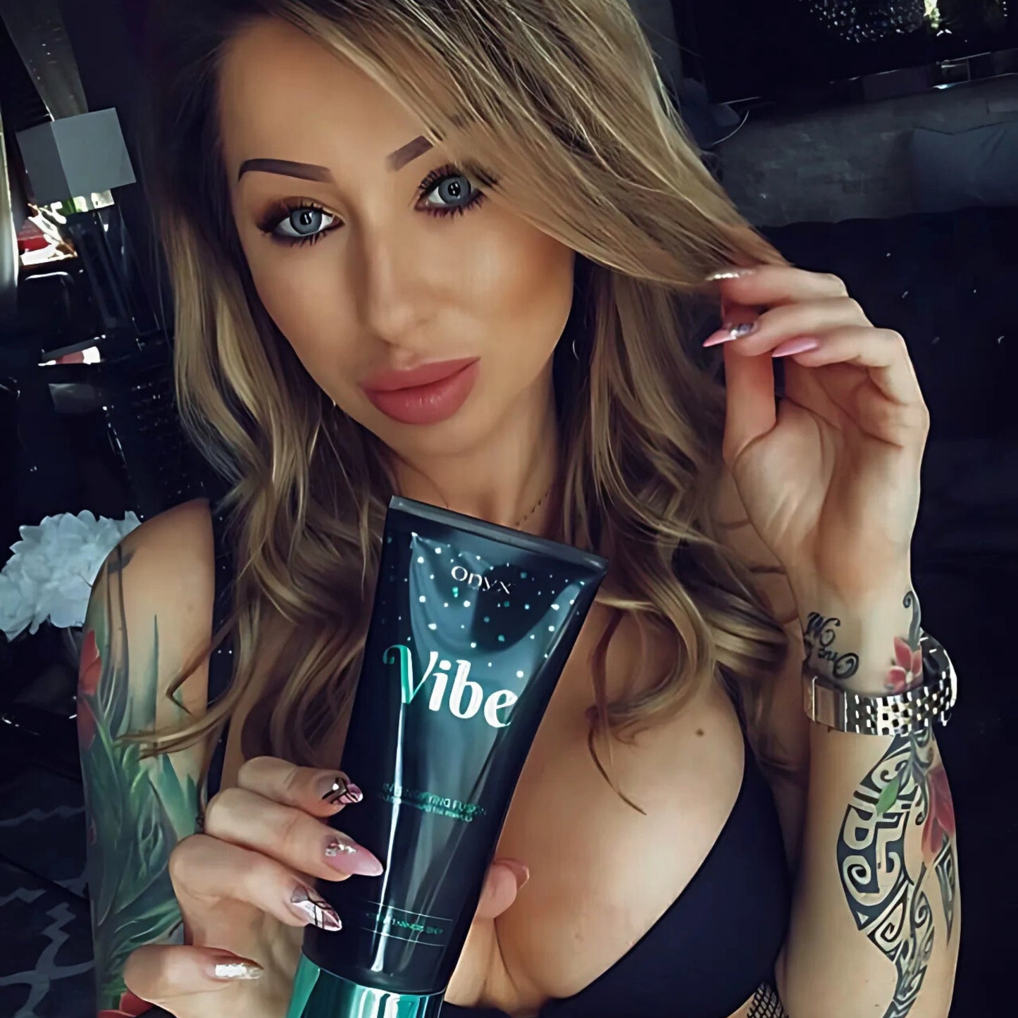 Frau mit Tattoos hält die Onyx Vibe Bräunungslotion in der Hand – gezielte Pflege für gebräunte Haut mit individuellem Stil
