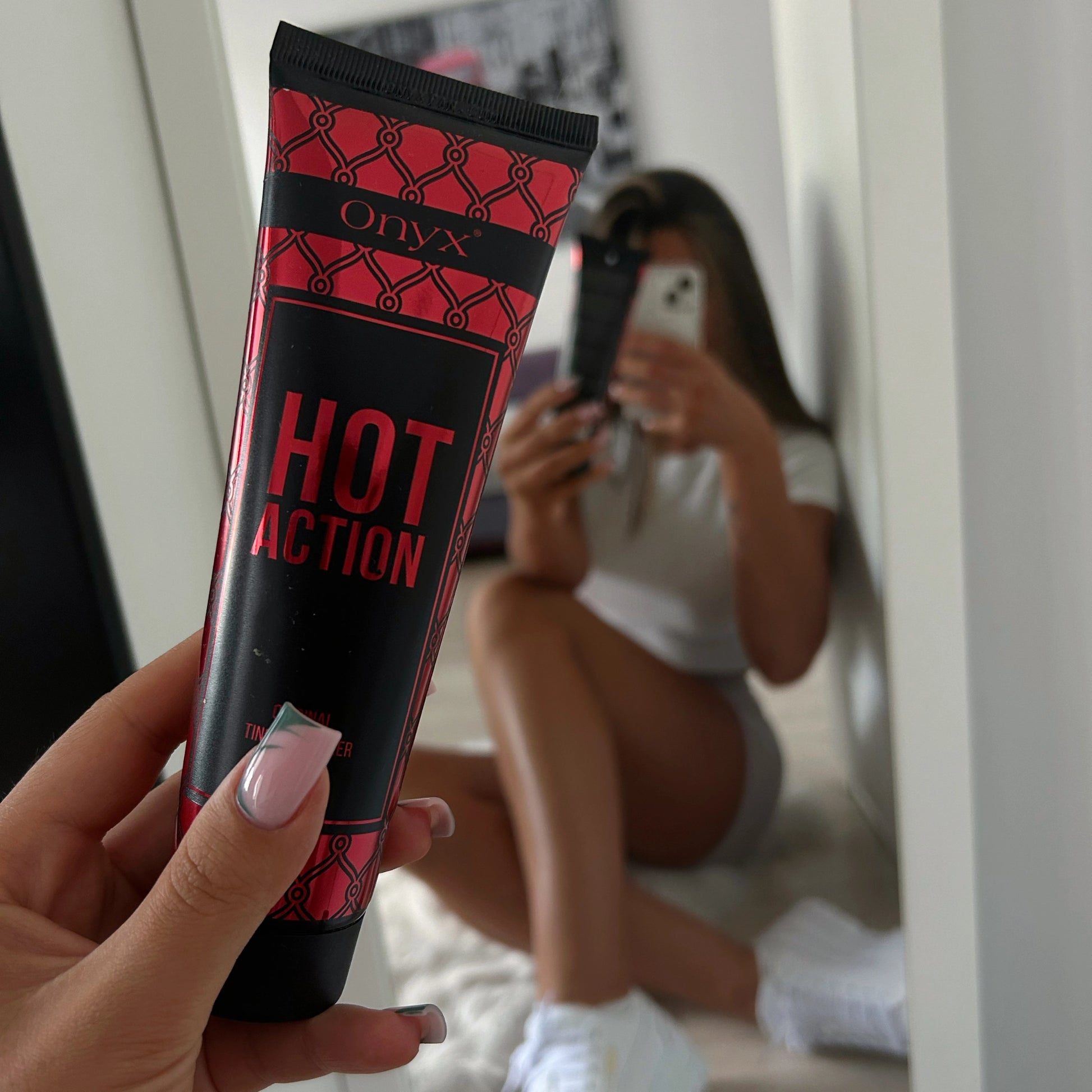 Frau macht Selfie im Spiegel während sie Onyx Hot Action Tingle Bronzer in der Hand hält, Fokus auf Produkt
