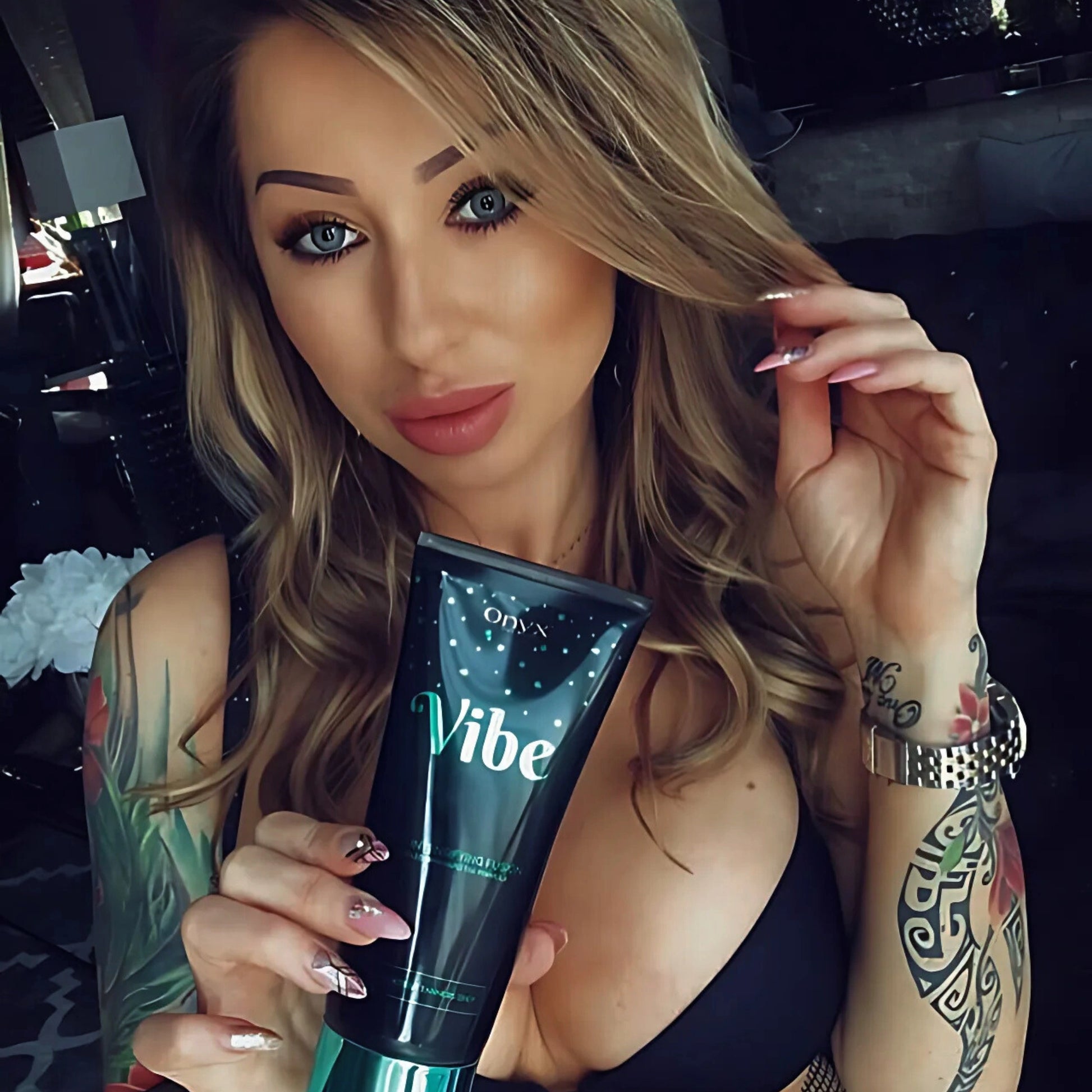 Frau mit Tattoos hält die Onyx Vibe Bräunungslotion in der Hand – gezielte Pflege für gebräunte Haut mit individuellem Stil