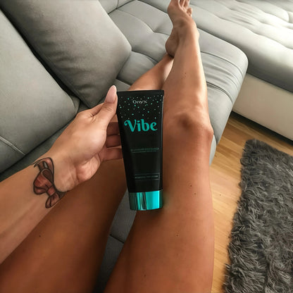 Entspannte Aufnahme einer Frau mit gebräunten Beinen und Onyx Vibe Lotion auf dem Sofa – sichtbar glatte, sommerlich gebräunte Haut